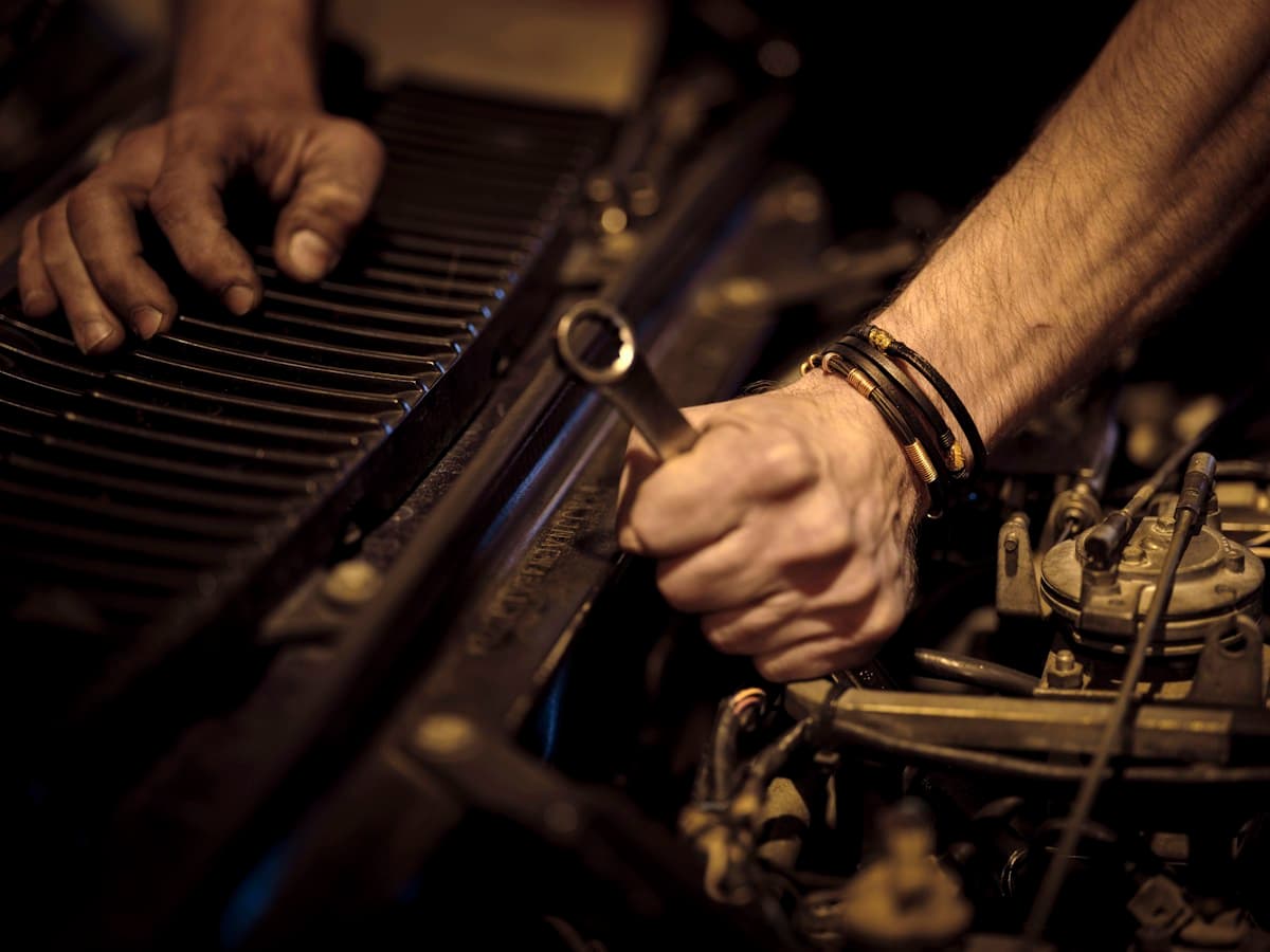 Mechanic's hands with grease working directly on engine bay components with wrench